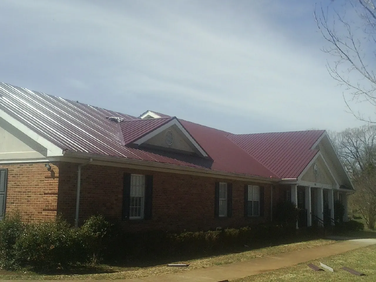Red metal roof with gabled entries on a long brick building, from a Hail Damage Roof Repair job in Carlisle