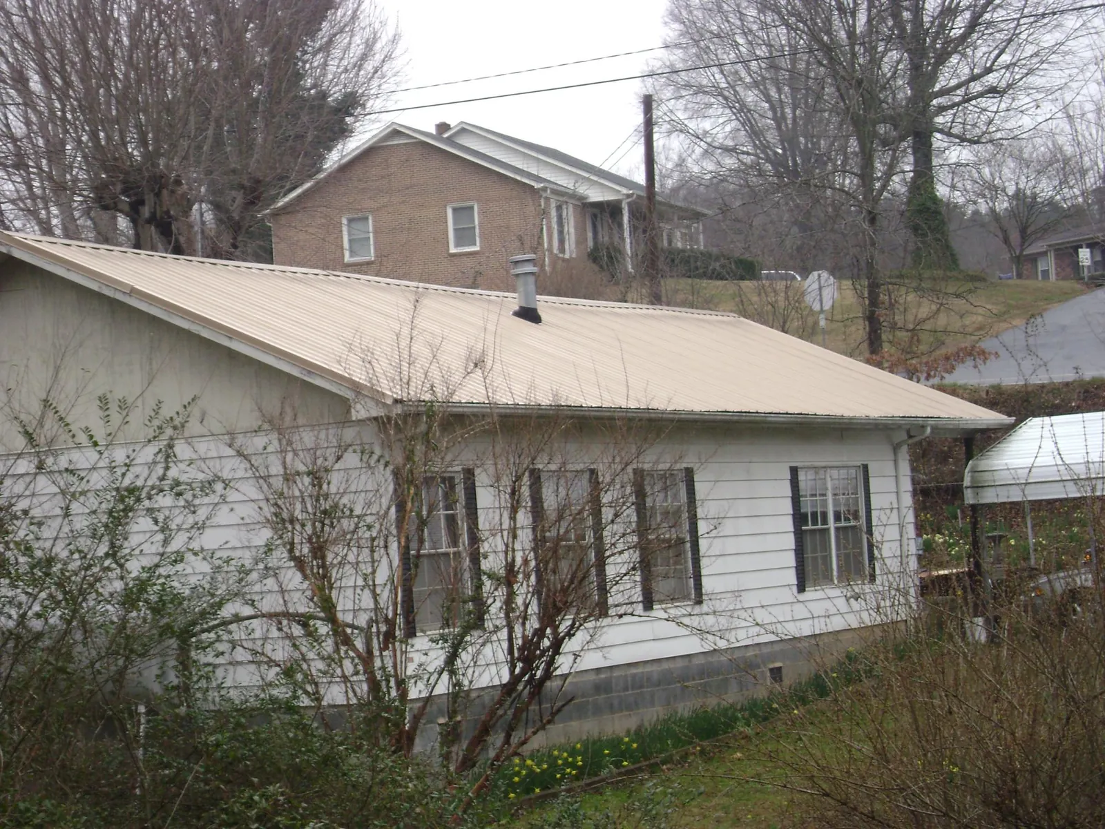 Tan metal roof on a white sided house set into a hillside — Commercial Roofing by Roofing Brothers in Carlisle